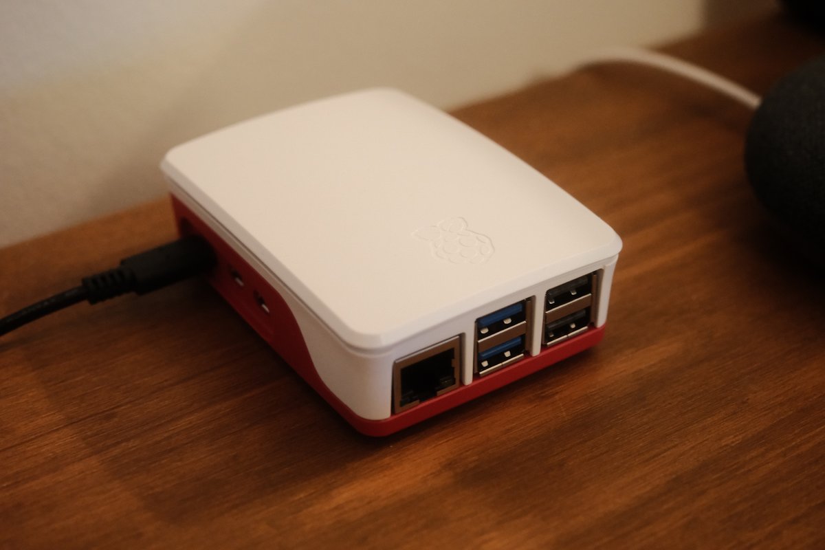 Raspberry Pi 5 in the official red and white case on a wooden desk, USB-C power connected